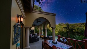 An outdoor patio with a table and chairs, a ceiling fan, and a view of the night sky. - Spectacular Hilltop Rental for 2 w/ Private Beach, Mountain & Sea Views. (Roatan)