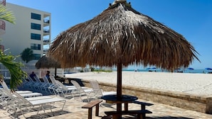 Eine Strandlounge mit reetgedeckten Sonnenschirmen, Liegestühlen und einem Tisch.