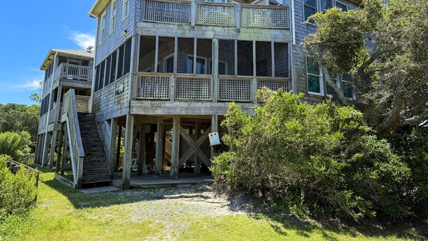 A two-story wooden house with a balcony, surrounded by greenery. - Ms Joy Bell:  Pet friendly, decks, screened porches, distant waterview (Ocracoke)