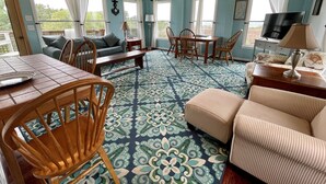 A room with a dining table, chairs, a sofa, a TV, and a patterned carpet. - Ms Joy Bell:  Pet friendly, decks, screened porches, distant waterview (Ocracoke)