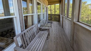 A wooden porch with benches and large windows overlooking a wooded area. - Ms Joy Bell:  Pet friendly, decks, screened porches, distant waterview (Ocracoke)