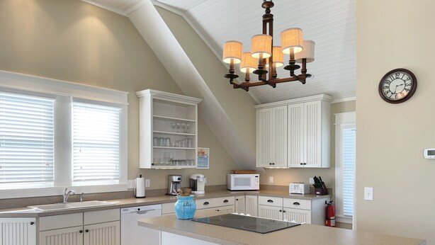 A kitchen with white cabinetry, a central island with stools, a chandelier, and a clock on the wall.