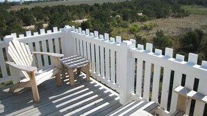 A wooden deck with a white picket fence, a Adirondack chair, and a small table.