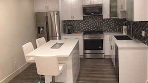 A modern kitchen with white cabinets, a stainless steel refrigerator, a microwave, a stove, and a coffee maker.