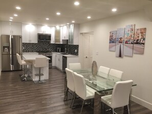 A modern kitchen with a refrigerator, stove, microwave, and a dining area with a glass table and white chairs.