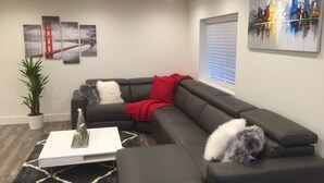 A modern living room with a sectional sofa, a white coffee table, a potted plant, and artwork on the walls.