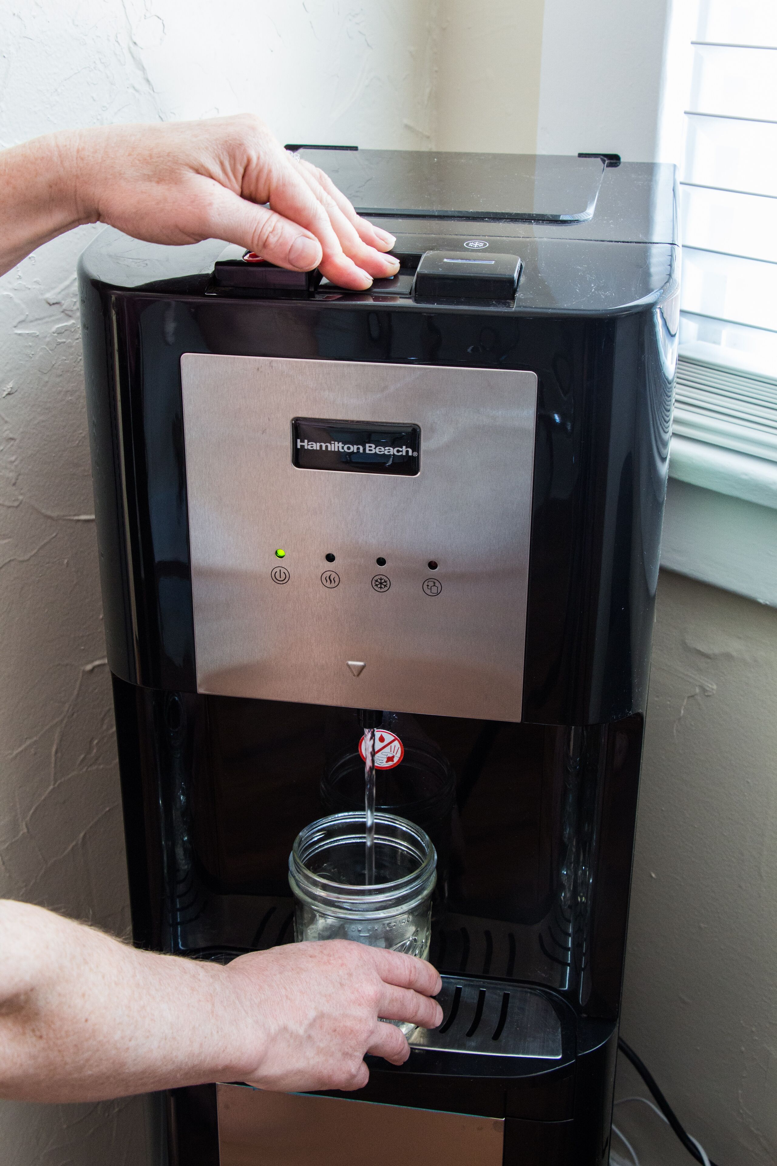 A water dispenser with a button and a glass jar below it.