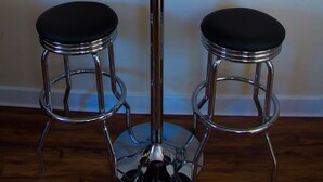 Una mesa redonda con dos taburetes, una vela encendida y un letrero en la pared que dice 'Eat'.