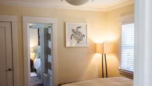 Un dormitorio con una cama, una obra de arte de una tortuga enmarcada, una lámpara de pie y un ventanal con persianas.