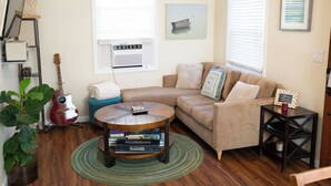 Una sala de estar acogedora con un sofá seccional, una mesa de centro con libros, una guitarra y una planta en maceta.