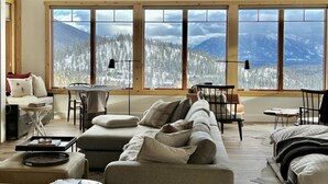 A cozy living room with a large window offering a mountain view. There is a sofa, a small table, and a chair. - Beautiful Ski-In/Ski-Out Penthouse (Whitefish)