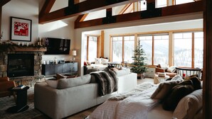 A cozy living room with a fireplace, large windows, and a view of the mountains. - Beautiful Ski-In/Ski-Out Penthouse (Whitefish)