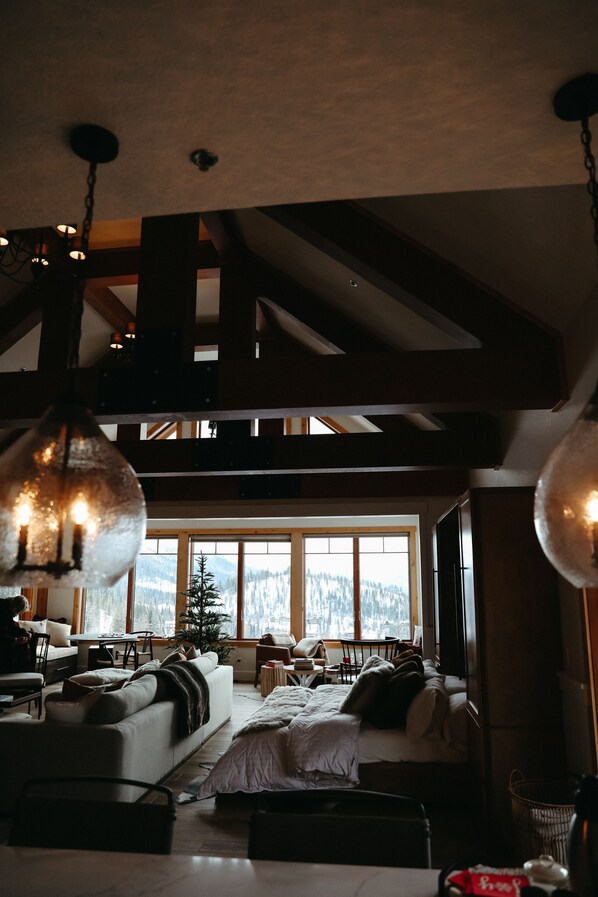 A cozy living room with a fireplace, large windows, and a high ceiling with exposed beams. - Beautiful Ski-In/Ski-Out Penthouse (Whitefish)
