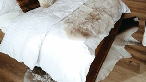 A bedroom with a large bed, wooden beams, a kitchen in the background, and a dining area with chairs. - Beautiful Ski-In/Ski-Out Penthouse (Whitefish)