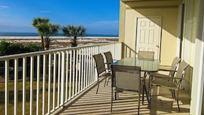 Ein Balkon mit Glastisch und Stühlen, der Blick auf einen Strand mit Palmen und einem strahlend blauen Himmel bietet.