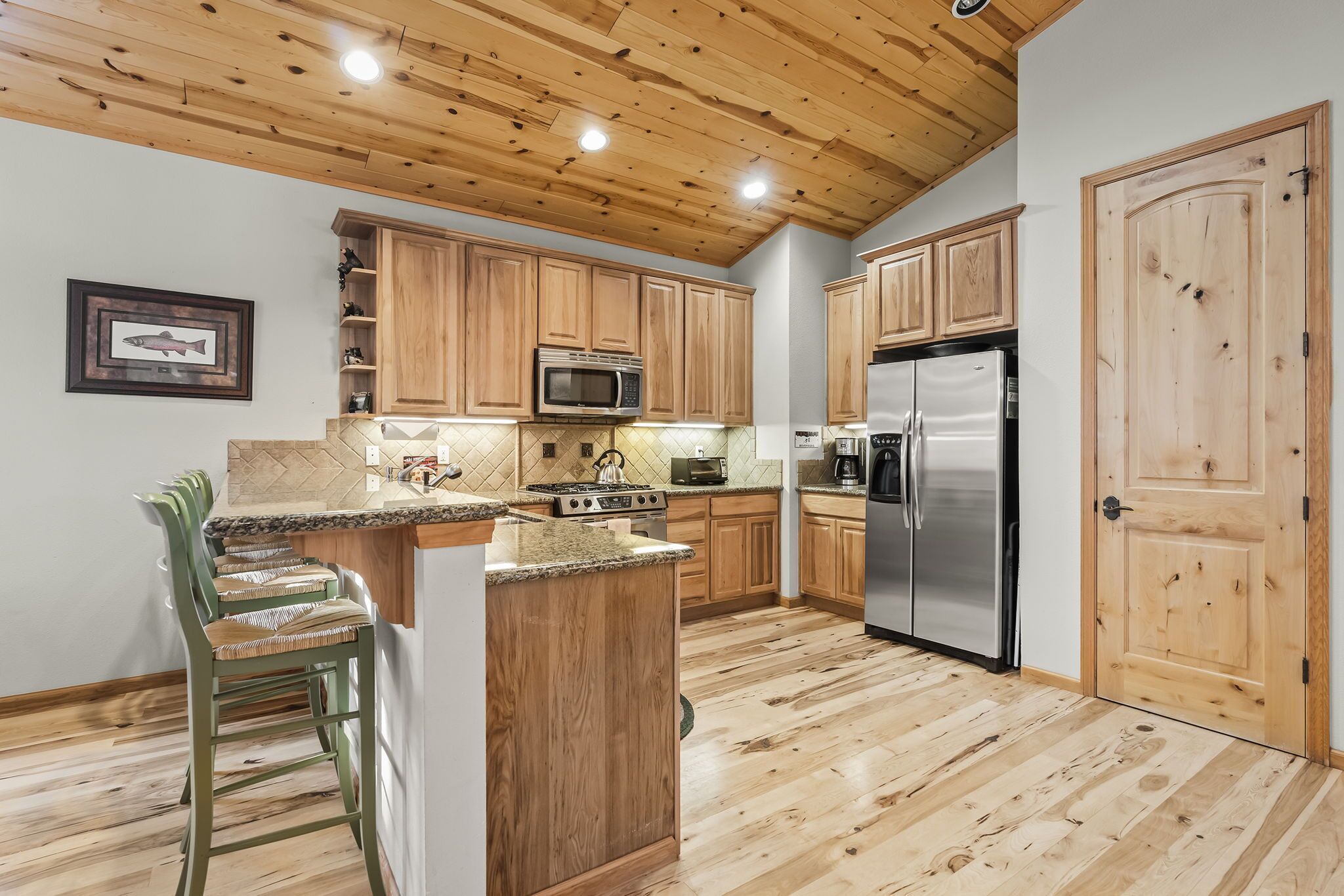 A kitchen with wooden cabinets, a stainless steel refrigerator, a microwave, and a wooden ceiling.
