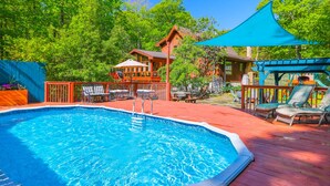 A swimming pool with a wooden deck, lounge chairs, and a gazebo.