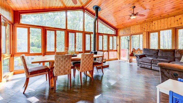 A spacious room with a wooden ceiling, large windows, a dining table with chairs, and a sofa.