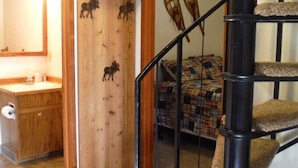 Un escalier avec une rampe noire et des marches recouvertes de moquette, menant à une chambre à coucher où le couvre-lit est à carreaux.