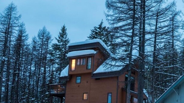 Une cabane en bois à plusieurs étages, dont le toit est recouvert de neige, et qui est entourée de grands pins.