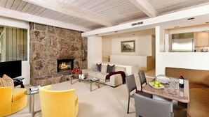 A living room with a stone fireplace, yellow armchairs, a sofa, and a dining area with a table set for two.