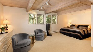 A bedroom with a bed, a TV, a desk with a lamp, and a chair.