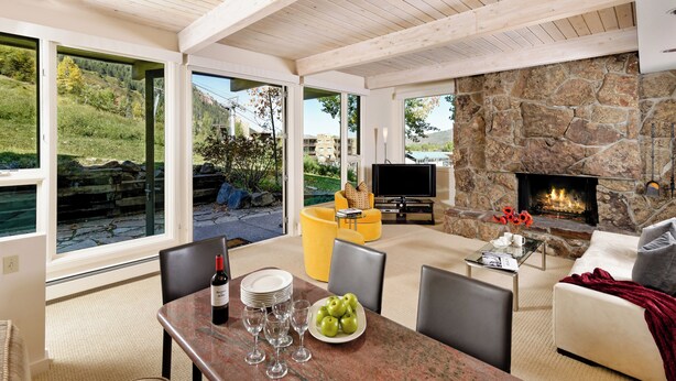 A spacious living area with a stone fireplace, a television, and a dining table with wine glasses and apples.