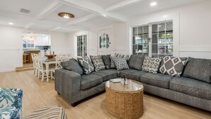 Una sala de estar moderna con un sofá seccional gris, una mesa de centro redonda y un comedor con sillas blancas y una mesa de madera.
