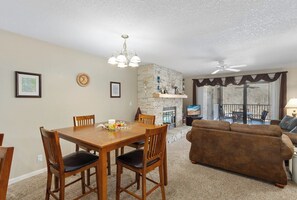 Un coin repas avec une table et des chaises en bois, une cheminée en pierre et un salon avec un canapé marron et un téléviseur.