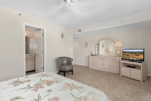 A bedroom with a bed, a chair, a dresser, a television, and a ceiling fan.