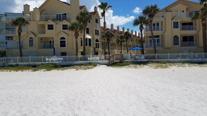 A beachfront hotel with multiple balconies, palm trees, and a sandy beach.