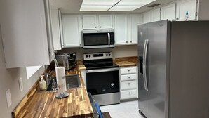 A modern kitchen with white cabinets, stainless steel appliances, a wooden countertop, and a skylight above.