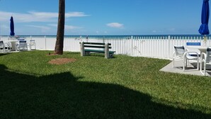 A beachside patio with a white fence, a bench, and tables with chairs.
