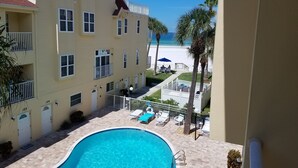 A hotel with a pool, a beach view, and a fenced patio area with lounge chairs.