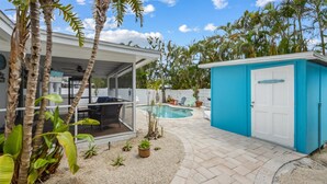 Un jardin avec une piscine, une terrasse couverte et un abri de jardin bleu.