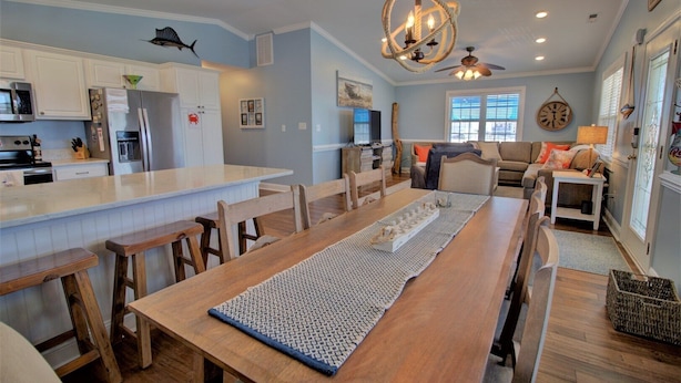 Une cuisine spacieuse dotée d’un îlot central, d’une table à manger en bois et d’un coin salon confortable avec un canapé et une horloge au mur.