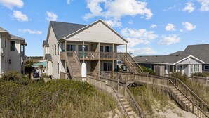 Ein Strandhaus mit einer Holzterrasse und einer Treppe, die zu einem Balkon führt.