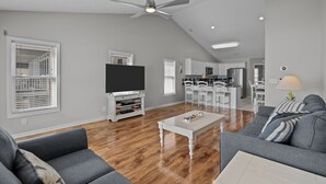 Ein geräumiges Wohnzimmer mit Fernseher, Deckenventilator und Essbereich mit weißen Stühlen.