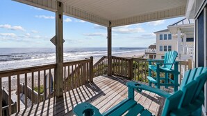 Eine Holzterrasse mit Blick auf Strand und Meer, ausgestattet mit Geländer und einigen Stühlen.