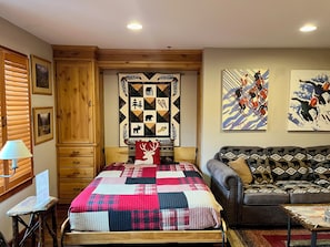 A cozy bedroom with a wooden bed, a quilt, a sofa, and a wall with a quilt and two paintings.