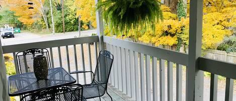 A covered outdoor area with a table and chairs, a hanging light fixture, and a view of yellow foliage.