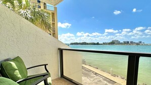 A balcony with a view of the sea, a chair, and a building in the background.