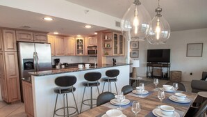 A modern kitchen with a central island, bar stools, and a dining table set for six with wine glasses and plates.