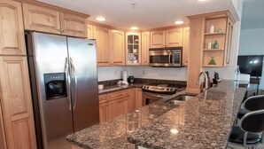 A modern kitchen with granite countertops, stainless steel appliances, wooden cabinets, and a built-in microwave.