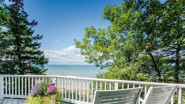 A wooden deck with a white railing, two white chairs, and a potted plant with flowers. - 2027 NOW OPEN!  Colossal Lakefront Home in Sawyer! (Sawyer)