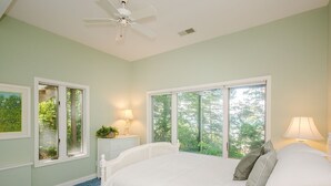 A bedroom with a large bed, two windows, a ceiling fan, and a nightstand with a lamp. - 2027 NOW OPEN!  Colossal Lakefront Home in Sawyer! (Sawyer)