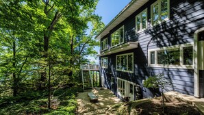 A two-story house with a covered porch, surrounded by lush greenery and trees. - 2027 NOW OPEN!  Colossal Lakefront Home in Sawyer! (Sawyer)