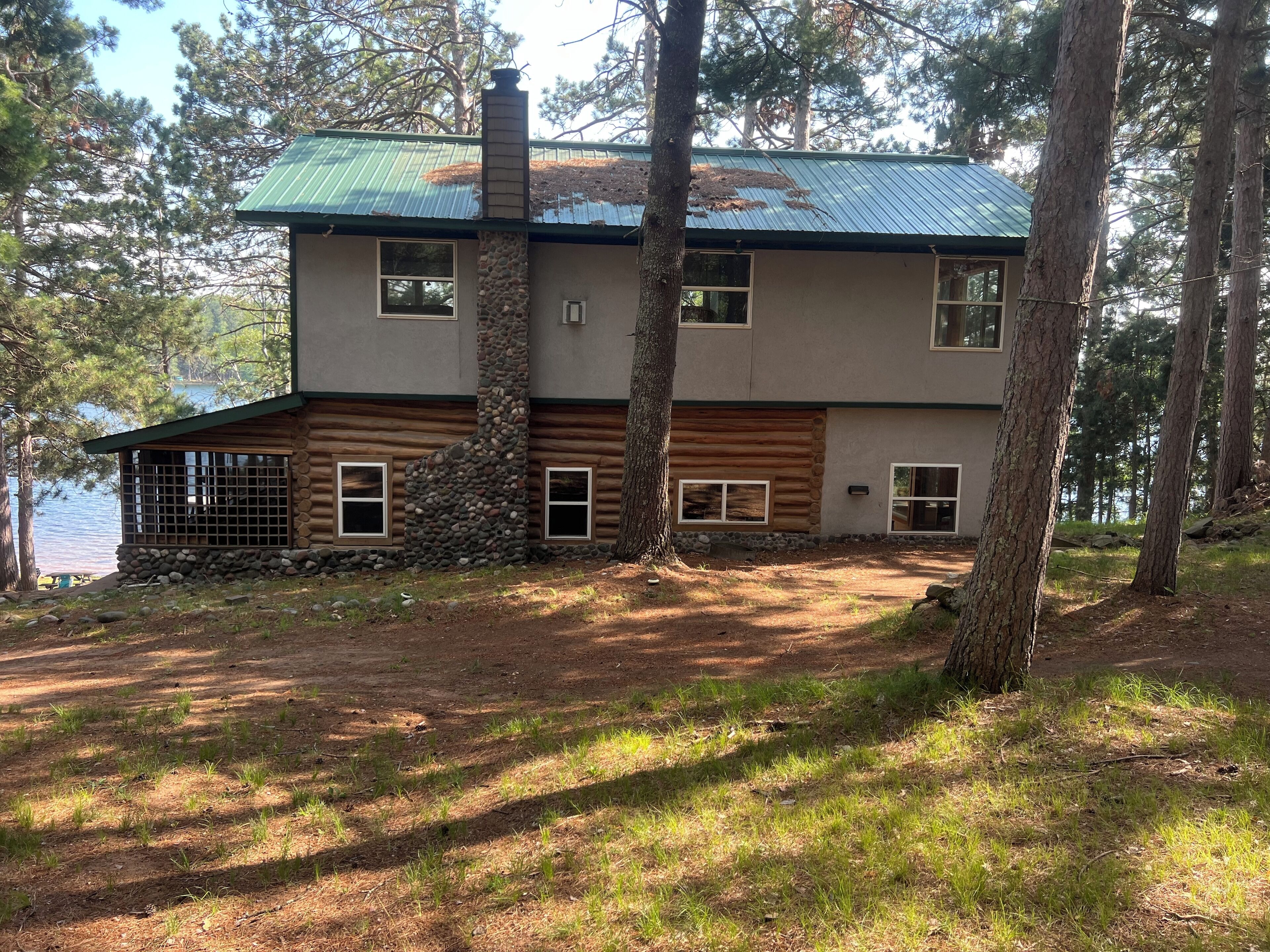Une cabane en rondins à deux étages, surmontée d’un toit en métal, située au bord d’un lac entouré d’arbres.