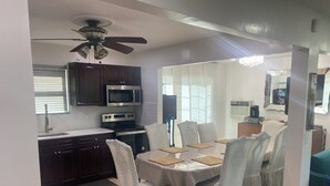 A modern kitchen with dark wood cabinets, a stainless steel microwave, and an oven. There is a dining table with white chairs and a rug. - 4 BR. 2 BTH, HOT TUB, MINS TO JONES BEACH, MINS TO RIVIERA WALK TO TRAIN TO NYC (Massapequa)