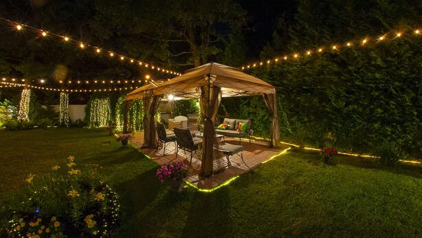A covered outdoor seating area with string lights, a table, and chairs. - 4 BR. 2 BTH, HOT TUB, MINS TO JONES BEACH, MINS TO RIVIERA WALK TO TRAIN TO NYC (Massapequa)